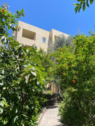 a building behind some bushes and trees with a pathway at Apartmani Agape in Petrovac na Moru
