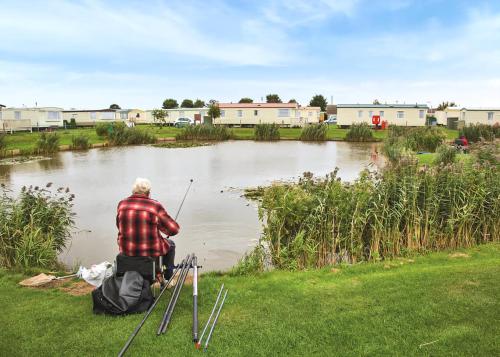 a man sitting on the grass fishing in a pond at Towervans Caravan Park in Mablethorpe
