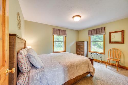 a bedroom with a bed and a chair and two windows at Ski, Hike and Fish Chalet with Hot Tub in Conway in Conway