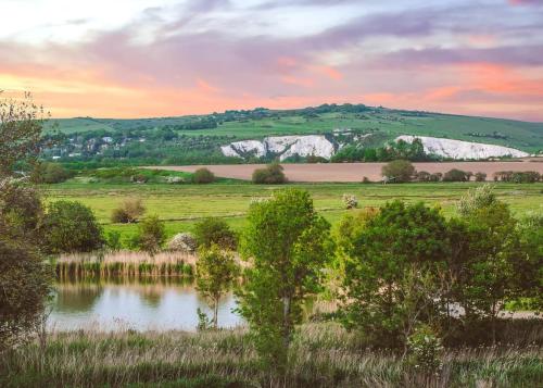 a view of a field with a lake and trees at Swanborough Lakes Luxury Lodges in Lewes