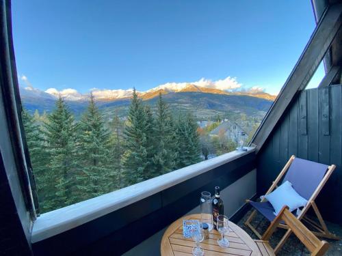 a table and a chair on a balcony with a large window at Le Duplex - Cosy & Vue Montagnes in Barcelonnette