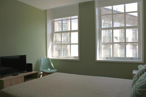 a bedroom with two windows and a bed and a chair at Alfred Studio in Guimarães