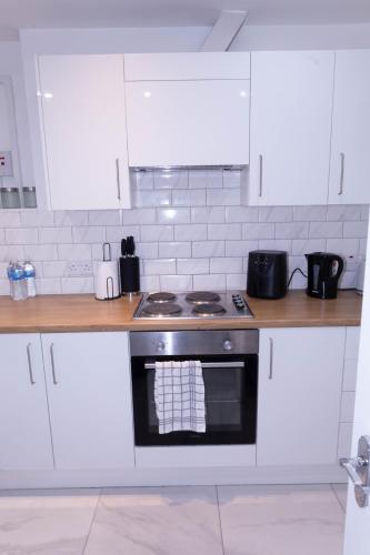 a kitchen with white cabinets and a stove top oven at Cosy 3 Bedroom Apartment Near The O2 in London