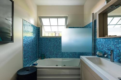 La salle de bains est pourvue d'une baignoire, d'un lavabo et de carrelage bleu. dans l'établissement VILLA ESCAPADES AU FERRET idéal Famille ou groupe d'Amis avec piscine chauffée 5 chambres Proche plages et pistes cyclables commerces Séjour paisible au cœur du Bassin d'Arcachon Nous répondons très rapidement aux demandes de renseignements, à Lège-Cap-Ferret