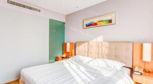 a bedroom with a large white bed with a wooden headboard at Tangshan Qiangang Hotel in Qian'an