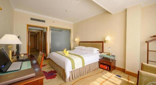 a bedroom with a bed and a desk with a computer at Quanzhou Overseas Chinese Hotel in Quanzhou