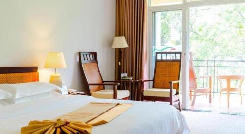 a bedroom with a bed and chairs and a balcony at Kunming Dianchi Garden Hotel & Spa in Kunming