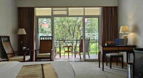 a bedroom with a bed and a desk and a balcony at Kunming Dianchi Garden Hotel & Spa in Kunming