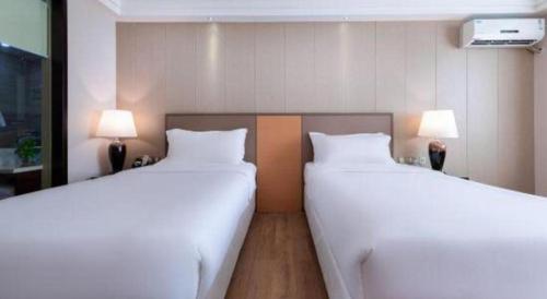 two white beds in a room with two lamps at Zhuhai Aqueen Hotel in Zhuhai
