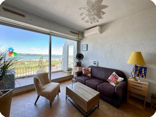 un salon avec un canapé et une grande fenêtre dans l'établissement Appartement 1ère ligne Vue mer, accès direct plage, à Palavas-les-Flots