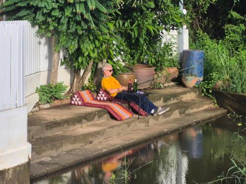 a man sitting on steps next to a body of water at 2 Fully equipped Cottages w big Pool & Fishing in Bang Sare