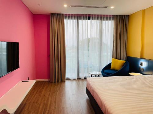 a hotel room with a bed and a tv and a chair at FLAMINGO Ibiza HaiTien - Ivy Abtel in Thanh Hóa