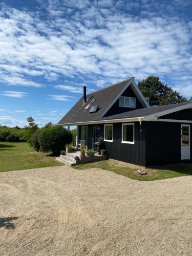 a black house with a gravel driveway at Hyggeligt Sommerhus med havudsigt in Humble