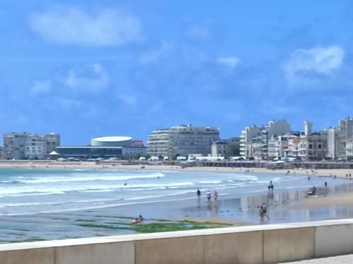 une plage avec des gens dans l'eau et dans les bâtiments dans l'établissement Appartement vue latérale mer proche marché Arago, à Les Sables-dʼOlonne