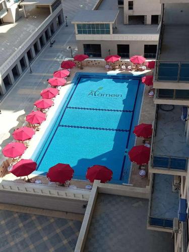 a swimming pool with red umbrellas and chairs at شقه فندقيه الداون تاون العلمين الجديده بجوار بالم هيلز والابراج in El Alamein