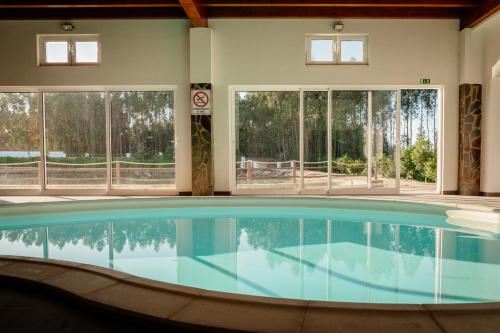 a large swimming pool in a building with windows at Herdade do Sardanito da Frente in Zambujeira do Mar