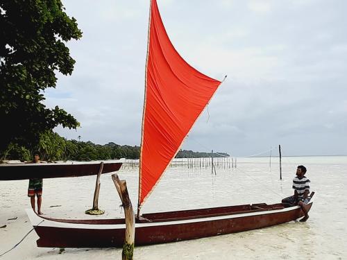 a person sitting on a boat with a red sail at Villa Maayun, a nest in paradise in Letman