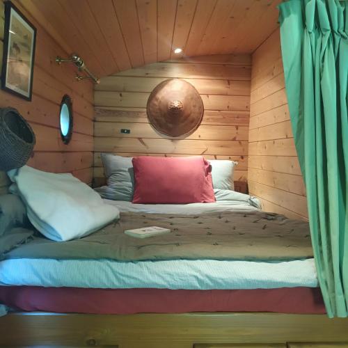 un lit dans une cabane en rondins avec un oreiller rouge dans l'établissement La Roulotte 4pl confort Au bord de la Rivière, à Laguépie
