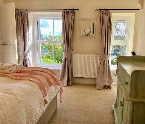 a bedroom with a bed and two windows at Key Cottage, sleeps 8 in Brimscombe