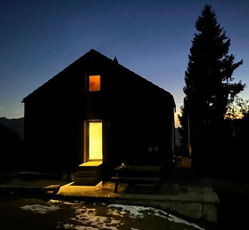 a black house with a lit window and a tree at Ca' Negra, Do-Minus Design Retreat & SPA in Bellinzona