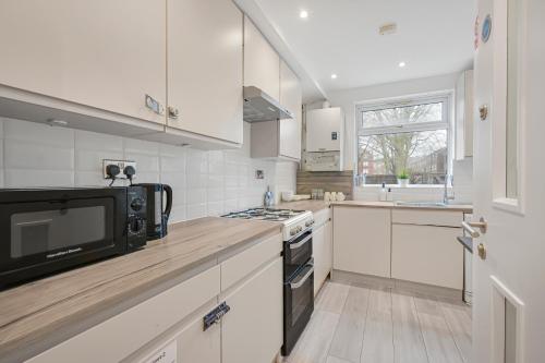 a kitchen with white cabinets and a black microwave at Bricklane Apartment in London
