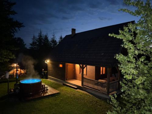 a log cabin with a hot tub in the yard at night at Domki Na Wzgórzu in Nowica