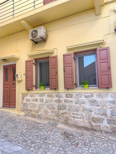 a building with red shutters and windows with plants at Pine Apartments in Ermoupoli