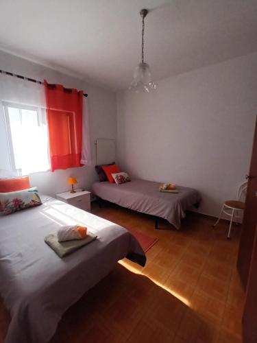 a bedroom with two beds and a window with red curtains at Casa marreiros in Aljezur