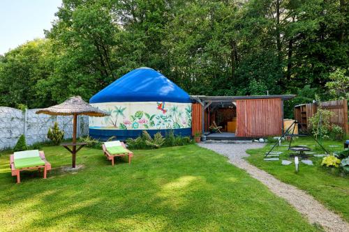 a tent in a yard with chairs and an umbrella at Aloha Glamp - okrągłe domki przy rzece - balia i sauna - Energylandia in Zagórnik