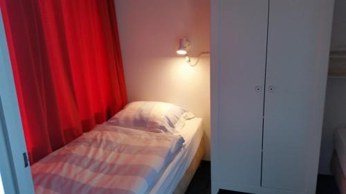 a small bedroom with a bed with a red curtain at DUINZICHT 6 Bed by the Sea in Westkapelle
