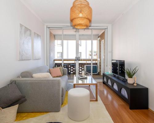 a living room with a couch and a tv at 1 min to the beach with A/C, balcony & parking in Sydney
