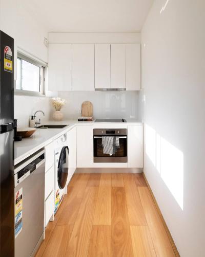 a kitchen with white cabinets and a wooden floor at 1 min to the beach with A/C, balcony & parking in Sydney