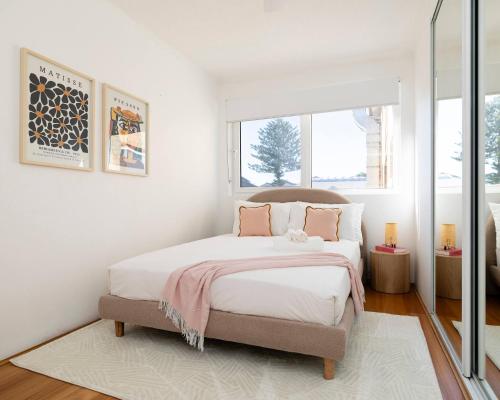 a bedroom with a bed with white sheets and pink pillows at 1 min to the beach with A/C, balcony & parking in Sydney