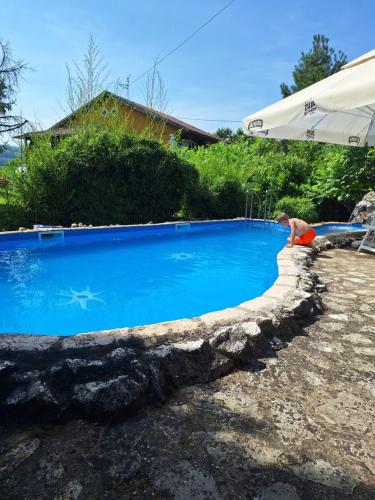 a man is sitting next to a blue swimming pool at Stara Vodenica in Klanjec
