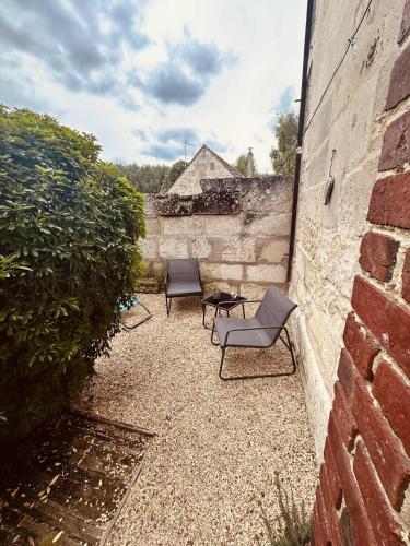 a patio with two chairs and a table next to a brick wall at gîte Cosy Green 2 in Chevincourt