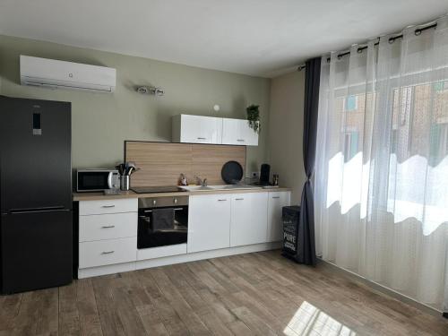 une cuisine avec des armoires blanches et un réfrigérateur noir dans l'établissement La Loge du Théâtre, à Orange