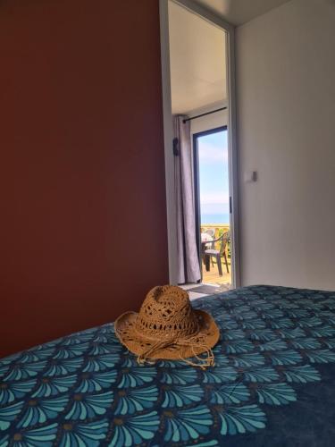 a straw hat sitting on a bed in a room at Mobil-home Vue mer Piscine - Camping La Falaise Equihen-Plage - La Coquille d'Opale in Équihen-Plage