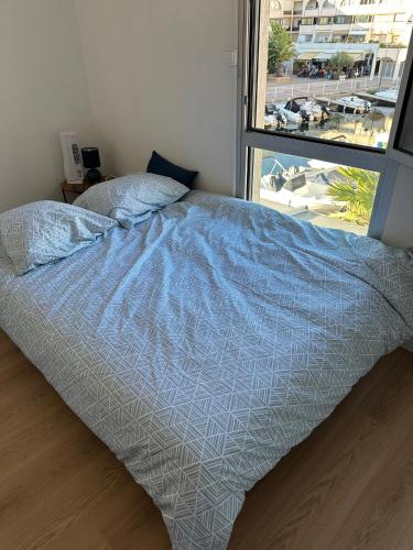- un lit avec une couette bleue dans une chambre dotée d'une fenêtre dans l'établissement Studette sur la Marina, plage à 5 minutes, à Sète