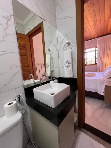 Un baño con un lavabo blanco y una cama. en Pousada Chalé Santa Teresa, en Santa Teresa