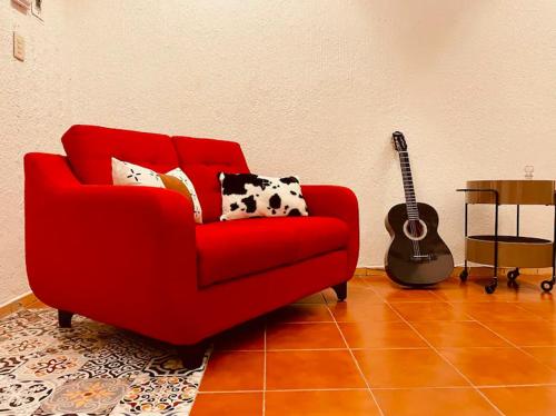 a red couch in a living room with a guitar at Bugambilia Azul Centro Oaxaca in Oaxaca City