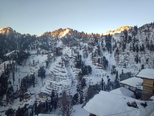 a mountain covered in snow with houses and trees at Boom shiva camps in Mandi