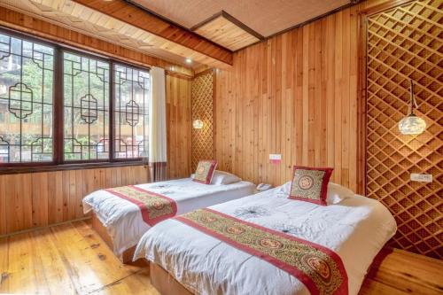 two beds in a room with wooden walls and windows at Longsheng Longji Rice Terraces Jingyue Hotel 龙胜龙脊梯田境悦酒店 in Longsheng