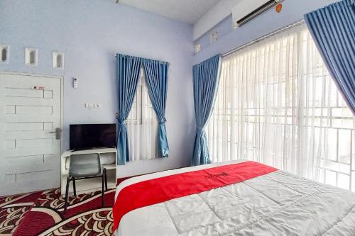 a bedroom with a bed and a television and blue curtains at RedDoorz Syariah at Masrun Homestay Bangkinang in Bangkinang
