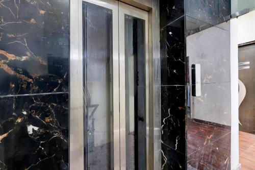 a glass shower door in a bathroom with black marble at Hotel O Rajeev Nagar Faridabad in Faridabad