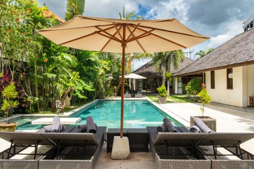 an umbrella and chairs next to a swimming pool at Villa Alroda Antik - Peaceful 4BR Villa with Private Pool in Canggu in Dalung