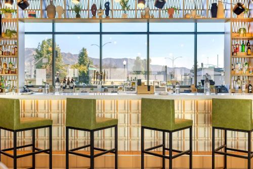a bar in a restaurant with two green chairs at Cambria Hotel Burbank Airport in Burbank