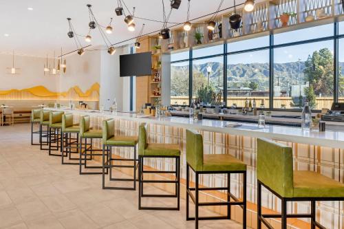 a row of green chairs at a bar in a restaurant at Cambria Hotel Burbank Airport in Burbank