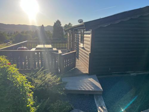 a wooden deck next to a house with the sun shining at Home From Home LogCabin in Trawsfynydd