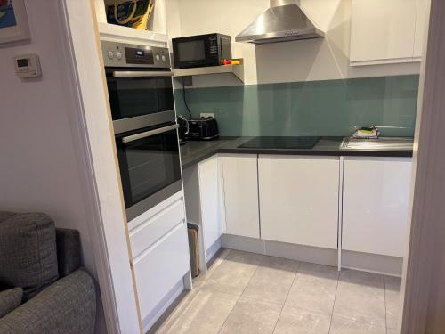 a small kitchen with white cabinets and black appliances at Seafront Sheringham 1 bed Apt sleeps 4 - 1xdog in Sheringham
