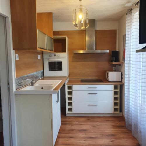 une cuisine avec des appareils électroménagers blancs et des armoires en bois dans l'établissement le nid des choups esprit cocoon 2 chambres, à La Bourboule